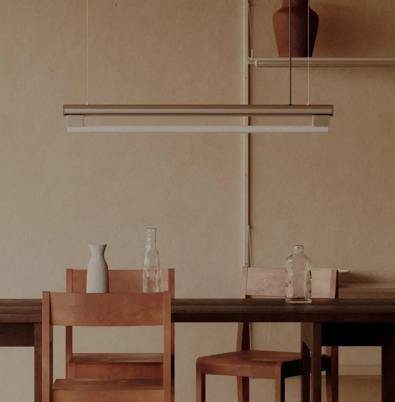 Wooden dining table with chairs, glass bottles and a pendant light in front of a warm clay wall